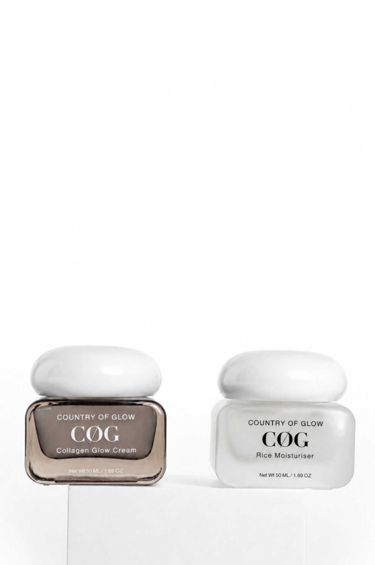 Two Country of Glow COG skincare jars on a white pedestal against a white background. The left jar is a square glass container with a white lid, containing Collagen Glow Cream in a brown-tinted bottle.