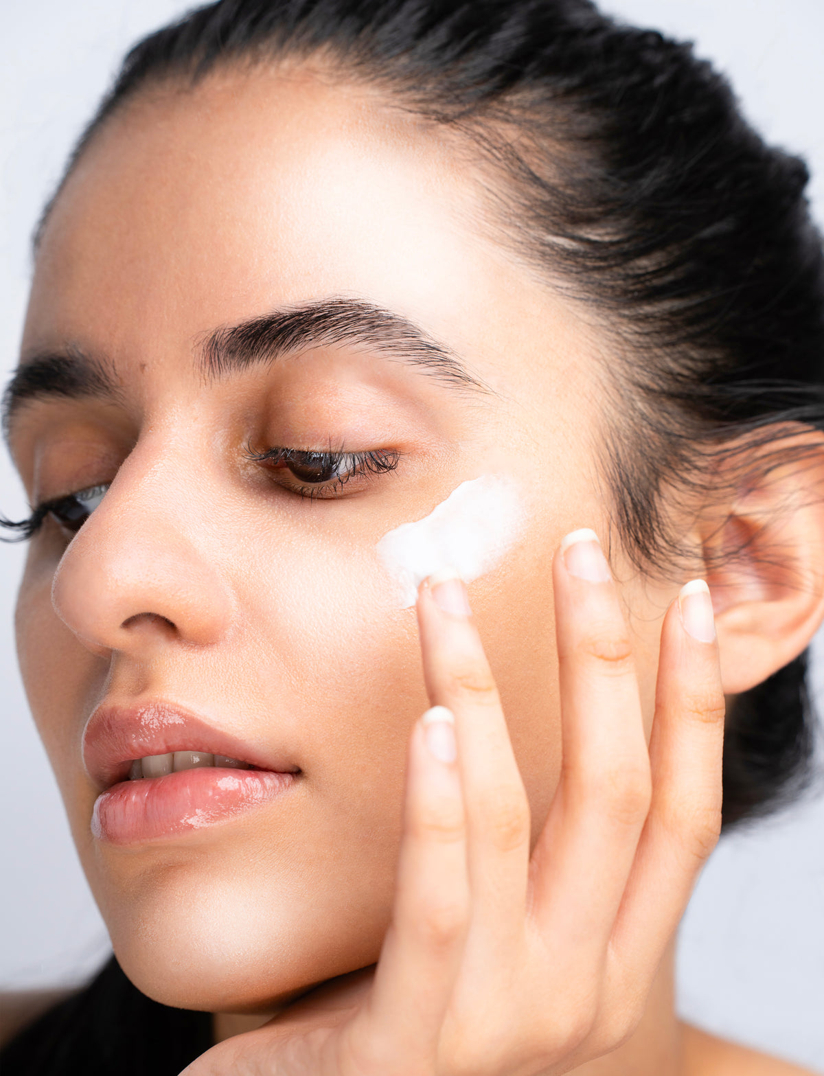 Woman applying cream to her face with a neutral background
